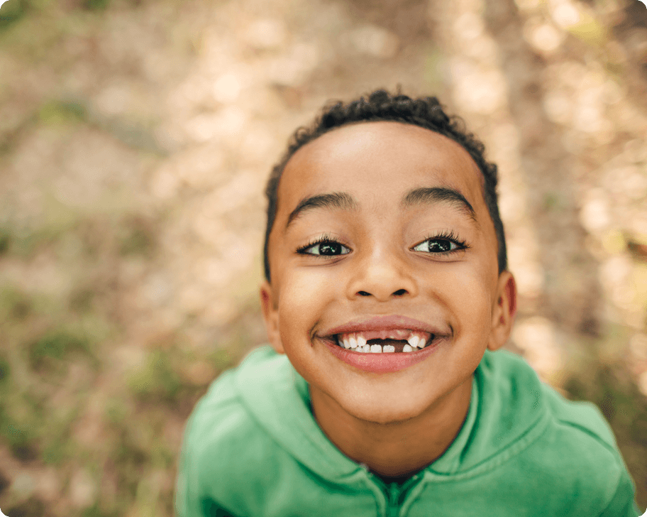 A boy missing teeth smiling into the camera.
